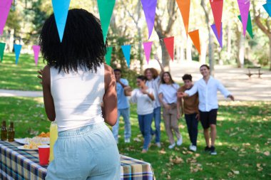 Kadın piknik masasının önünde duruyor, arkadaşlarının doğum günü partisine gelmesiyle şaşırmak üzere.