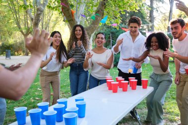 Neşeli gençler güneşli bir günde parkta bira pong oynuyorlar.