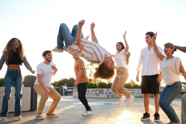 Group of friends having fun outdoor with a young man doing a backflip in the air in a sunny day clipart