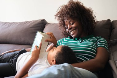 Gülümseyen anne oğluna kitap okurken o rahat bir kanepede yatıyordu.