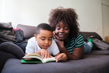 Anne ve oğlu evde oturup kanepede uzanmış kitap okuyorlar.