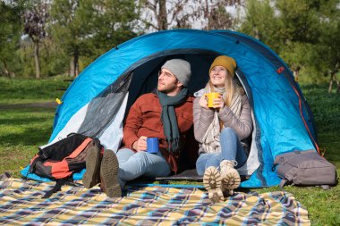 Genç çift ormanda kamp yaparken çadırlarında sıcak içeceklerin tadını çıkarıyor.