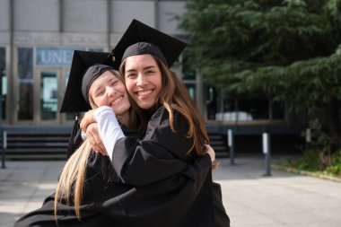 Üniversite binasının önünde sevinçle sarılan iki mezun.