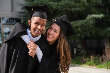 İki mezun başarılarını büyük bir gülümsemeyle kutluyor.