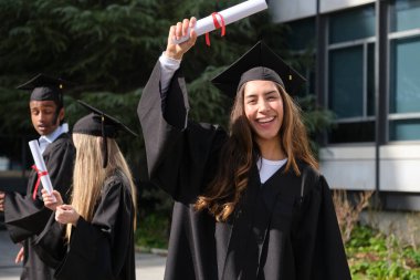 Mezuniyet derecesi alan mutlu bir öğrenci, arka planda sınıf arkadaşları var.