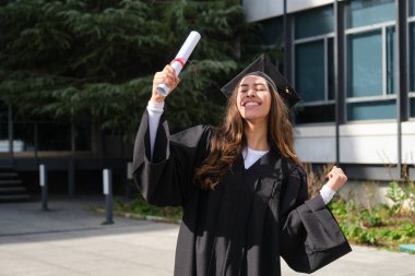 Üniversite binasının önünde diploma taşıyan mutlu mezun öğrenci.