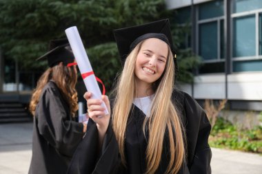 Diplomasını elinde tutan mutlu mezun öğrenci üniversitenin yakınındaki mezuniyet gününü kutluyor