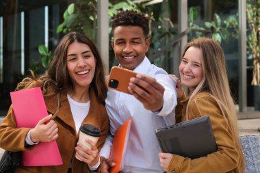 Bir grup neşeli çok ırklı üniversite öğrencisi dışarıda selfie çekiyor.