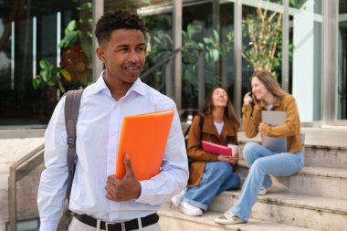 Üniversite binasının dışında yürüyen genç bir üniversite öğrencisi. Elinde bulanık sınıf arkadaşlarının olduğu bir dosya var. Arka planda oturup konuşuyorlar.