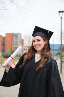 Diplomasını elinde tutan gülümseyen mezun bir öğrencinin portresi.