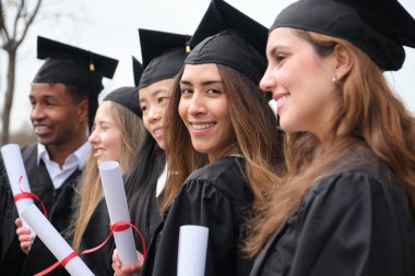 Mezuniyet töreninde diplomalarını elinde tutan bir grup neşeli çoklu etnik mezun.