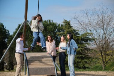 Neşeli çoklu etnik kökenli genç arkadaşlar parkta birlikte eğleniyorlar, açık havada güneşli bir günün tadını çıkarıyorlar.