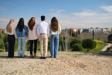 Güneşli bir günde parkın manzarasına hayran olan beş öğrenci.
