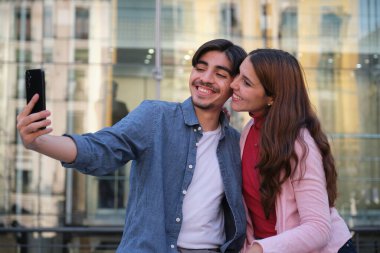 Genç çift gülerek ve akıllı telefonuyla selfie çekerek gün içinde şehir merkezinde