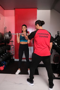 Modern spor salonundaki spor salonunda ağırlık kaldıran genç bir kadına yardım eden kişisel antrenör.