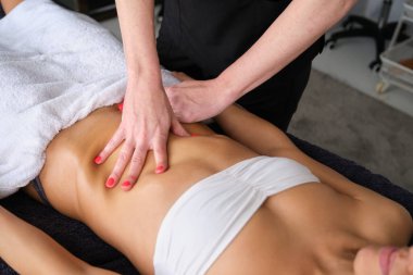 Profesyonel masöz masaj salonundaki masaj masasında yatan genç bir kadına karın masajı yapıyor.