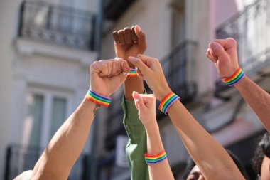 Eylemciler, LGBT onur yürüyüşünde gökkuşağı bilezikleri takarak yumruklarını kaldırıyorlar.