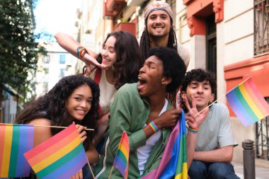 Bir grup mutlu çoklu etnik arkadaş LGBT onur geçidinde birlikte eğleniyor, gökkuşağı bayrakları sallıyor ve gökkuşağı bilezikleri takıyorlar.