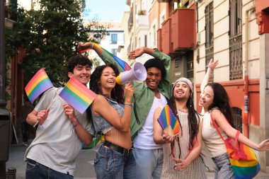 Bir grup arkadaş lgbt onur geçidinde eğleniyor, gökkuşağı bayrakları sallıyor ve megafon kullanıyorlar.