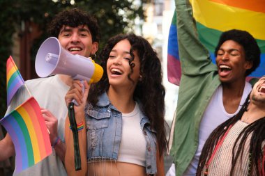 Bir grup genç aktivist ellerinde gökkuşağı bayrakları ve bir lgbt onur geçidine megafonla bağırıyorlar.