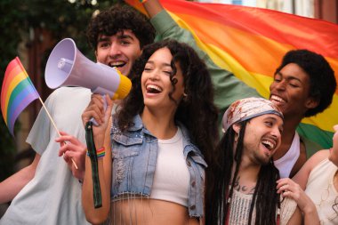 Bir grup mutlu çoklu etnik aktivist ellerinde gökkuşağı bayrakları ve megafonla bağırarak bir lgbt onur yürüyüşüne katılıyor.