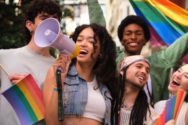 LGBT onur yürüyüşünde megafonla konuşan genç bir kadın gökkuşağı bayrakları sallayan arkadaşlarıyla