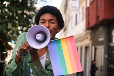 Elinde gökkuşağı bayrağı tutan ve megafon kullanan genç adam lgbt Onur Yürüyüşü 'nde eşit haklar ve özgürlüğü destekliyor.