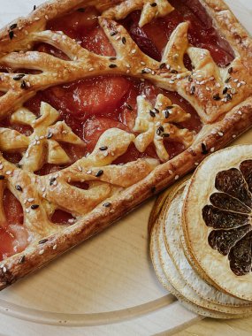 Homemade pie with jam, in the style of autumn comfort. A dried orange is laid out around the pie.