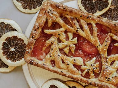 Homemade pie with jam, in the style of autumn comfort. A dried orange is laid out around the pie.