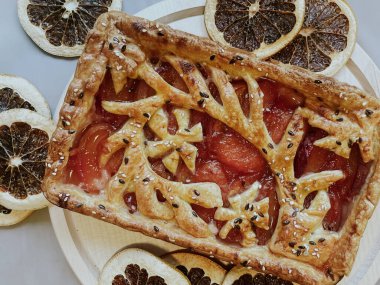 Homemade pie with jam, in the style of autumn comfort. A dried orange is laid out around the pie.