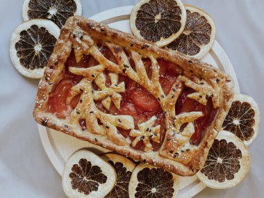 Homemade pie with jam, in the style of autumn comfort. A dried orange is laid out around the pie.