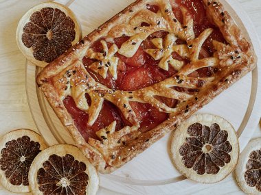 Homemade pie with jam, in the style of autumn comfort. A dried orange is laid out around the pie.
