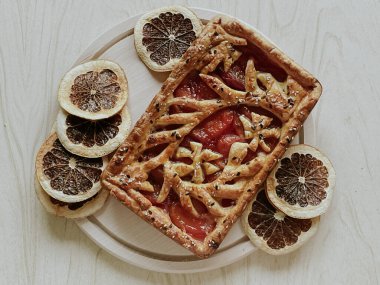 Homemade pie with jam, in the style of autumn comfort. A dried orange is laid out around the pie.