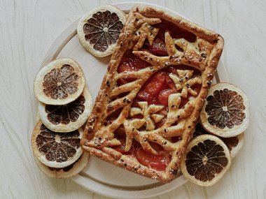 Homemade pie with jam, in the style of autumn comfort. A dried orange is laid out around the pie.