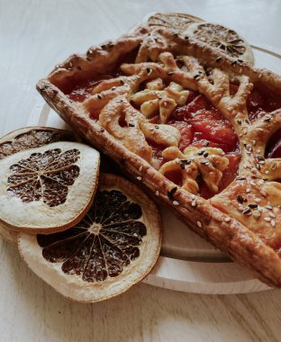 Homemade pie with jam, in the style of autumn comfort. A dried orange is laid out around the pie.