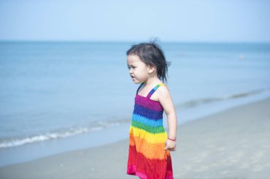 Yaz tatilinde sahilde oynayan bir kız, doğada güzel bir deniz, kum ve mavi gökyüzü olan bir çocuk, deniz kenarında tatilde olan mutlu bir çocuk, suda koşan..