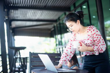 Bilgisayarlı Asyalı bir anne evden masa başında çalışıyor ve yanında küçük bir çocuk büyütüyor..