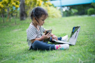 Asya aile pikniğin kutlu olsun. Kızlar cep telefonları ve dizüstü bilgisayarlarla oynuyorlar güneşli bir günde tek başlarına otururken eğleniyorlar..