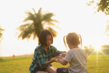 Güzel, sarı bir günbatımında arka bahçede çimlerin üzerinde oturan iki küçük kızın silueti..
