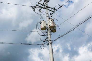Beton gri yuvarlak elektrik direği, enine kahverengi metal çerçeveler, yalıtkan kümeleri, ana elektrik yüksek gerilim kabloları, tetikleyici teller vasıtasıyla birbirine bağlı.