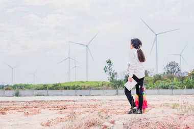 Asyalı kızlar elektrik üretmek için rüzgar türbinlerini incelerler. Sürdürülebilir enerji. gelecek.