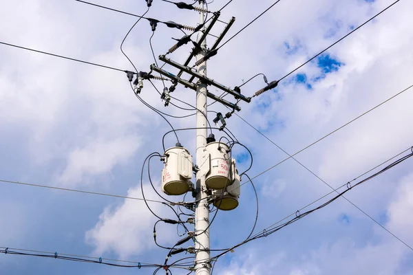 Beton gri yuvarlak elektrik direği, enine kahverengi metal çerçeveler, yalıtkan kümeleri, ana elektrik yüksek gerilim kabloları, tetikleyici teller vasıtasıyla birbirine bağlı.