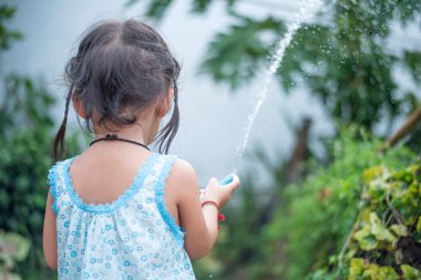 Genç bir kız çiçekleri hortumla ıslatıyor..