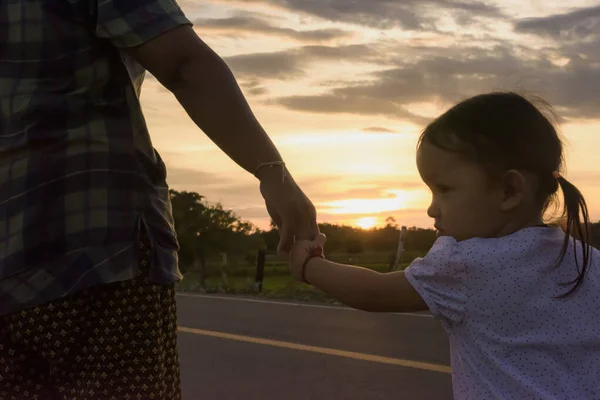 太陽が両親と子供を設定するときに母親の手を握っている子供は 日当たりの良い通りに立って互いに純粋な愛を示しています — ストック写真