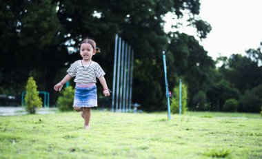 Sevimli küçük kız evde eğleniyor, etrafta koşuşturuyor ve çimlerin üzerinde zıplıyor. Mutlu çocuklar çocukluğun tadını çıkarıyor ve evde oynuyorlar..