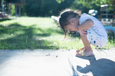 Asyalı küçük kız parkta oynamak için büyüteç kullanıyor.