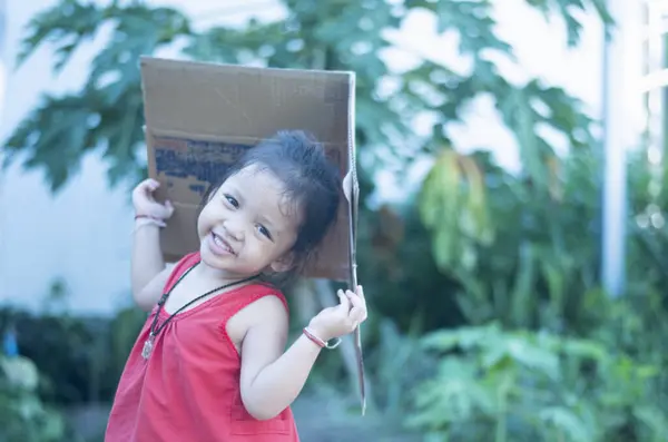 Clever girl plays with a box and holds pieces of paper above her head as a roof.