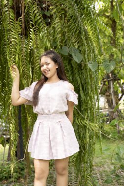 Gündelik giysiler içindeki güzel genç bir kadın yazın yeşil ormanda yürüyor ve kır çiçeklerine hayranlık duyuyor. Doğada aktif olan gençlerin boş zamanlarını değerlendiriyor..