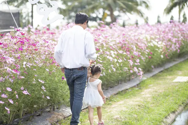 Little girl with her father on nature background A back view of the Father in Heaven concept. Father holds daughter\'s hand as she walks.