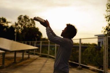 Orta yaşlı bir adamın silueti sabahın köründe güneşin doğuşuna karşı Tanrı 'ya dua ediyor. Kişinin elleri ibadet için kaldırılır. Tanrı tövbe etmeye yardım ediyor. Roma Katolikliği, Paskalya, Paskalya, Paskalya, Zihin, Dua, Hıristiyanlık konsepti.